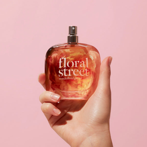 Hand holding  floral street Wonderland Peony 50ml perfume bottle against a pink background
