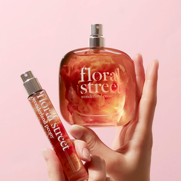 Hand holding a Floral Street Wonderland Peony vegan luxury gourmand perfume bottle and travel bottle on a pink background