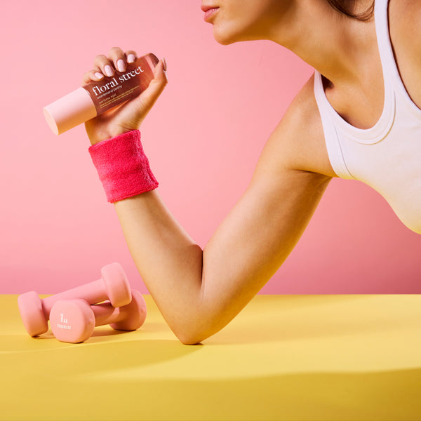 Woman exercising with pink dumbbells, holding a Floral Street Wonderland Peony Perfume Mist against a pink background