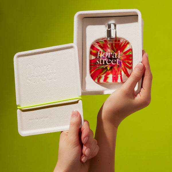 Floral Street perfume bottle in a white box held by hands against a green background